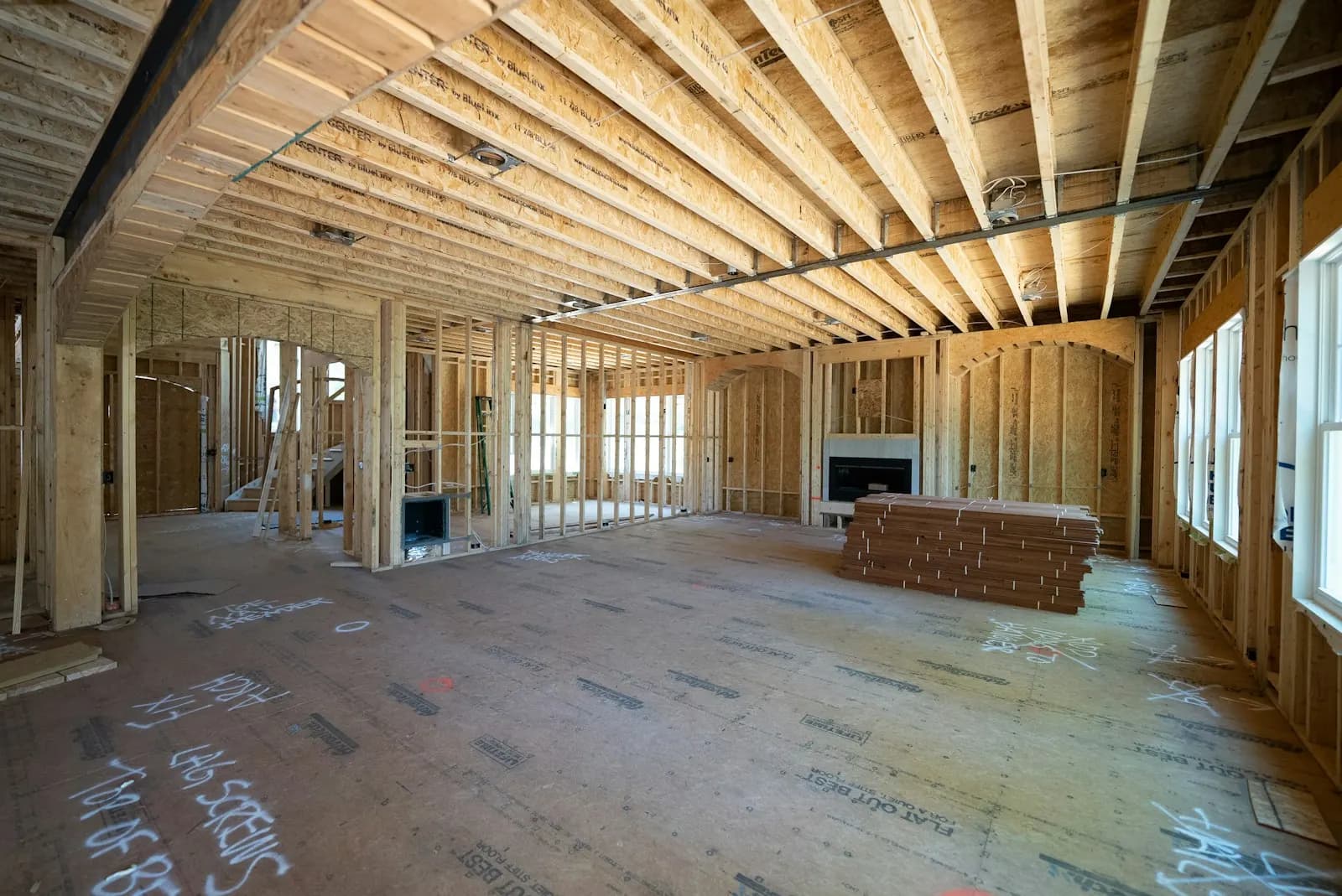 Intérieur d’une maison neuve en charpente de bois : colombages, solives au plafond et pile de panneaux sur le sous-plancher