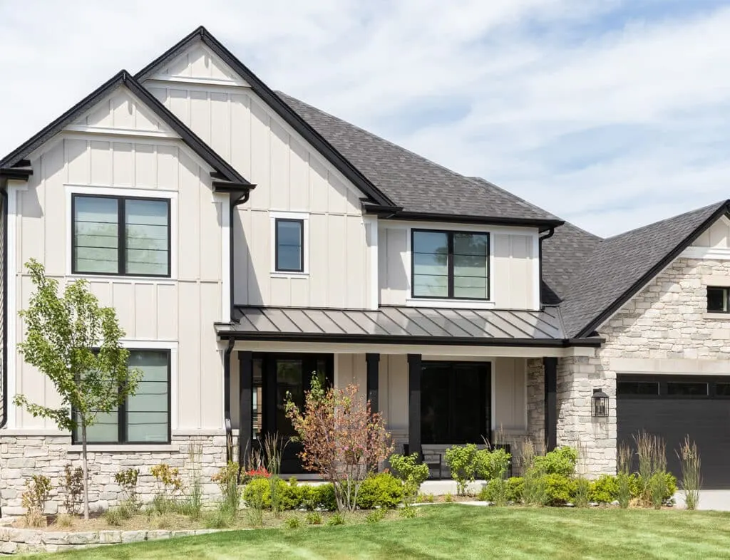 Beige board and batten siding paired with a natural stone base and a black roof