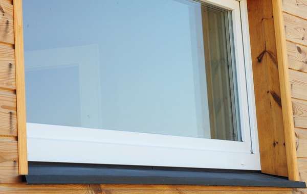Bas d’une fenêtre en PVC avec son solin noir et son cadre de bois vus de l’extérieur