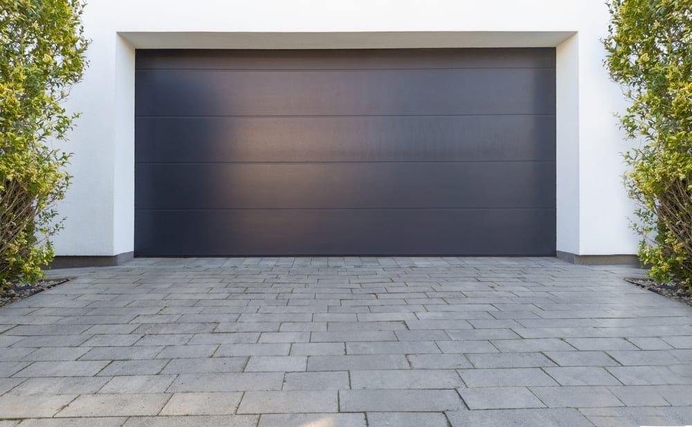 Porte de garage double en acier noir à panneaux lisses, sur une maison au revêtement blanc