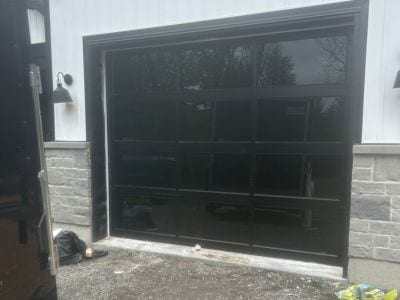 Porte de garage pleine vue à cadre d’aluminium noir et verre clair, sur une maison au revêtement blanc