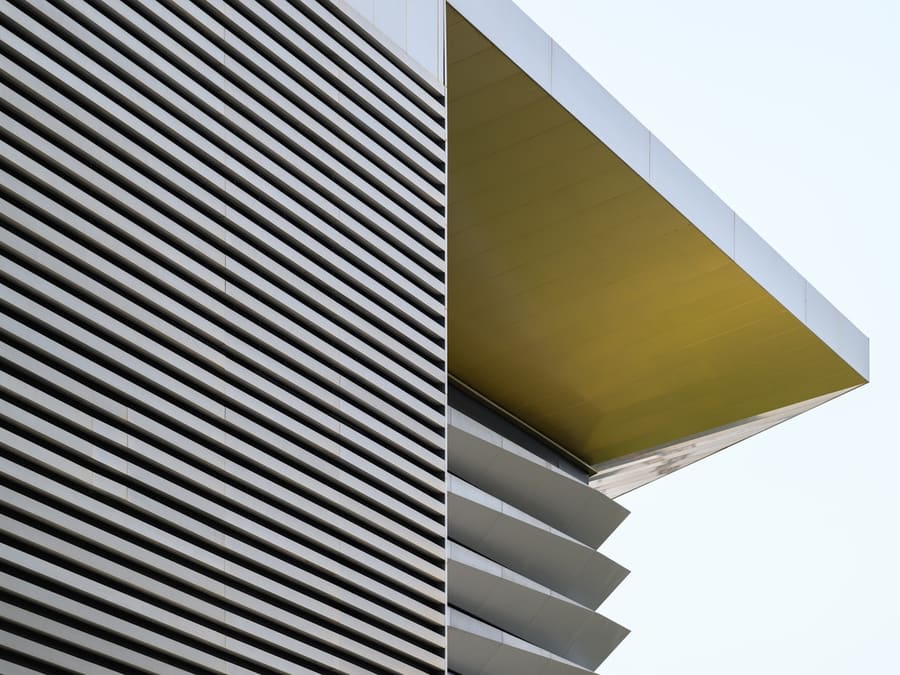 Mur extérieur en panneaux d’acier profilés foncés, avec un débord de toit à l’intrados jaune