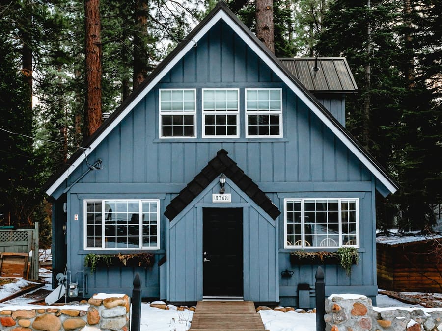 Maison de style chalet recouverte d’un revêtement vertical bleu de type board and batten, avec un soubassement de pierre