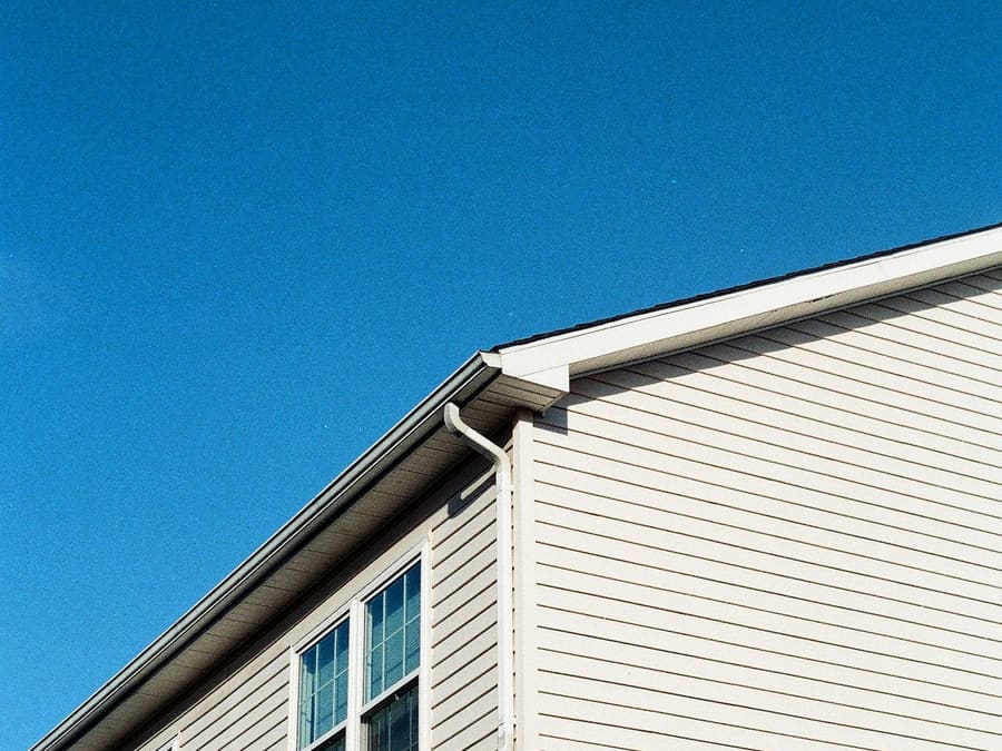 Pignon d’une maison recouvert d’un déclin horizontal blanc cassé aux lignes très nettes, sous un ciel bleu