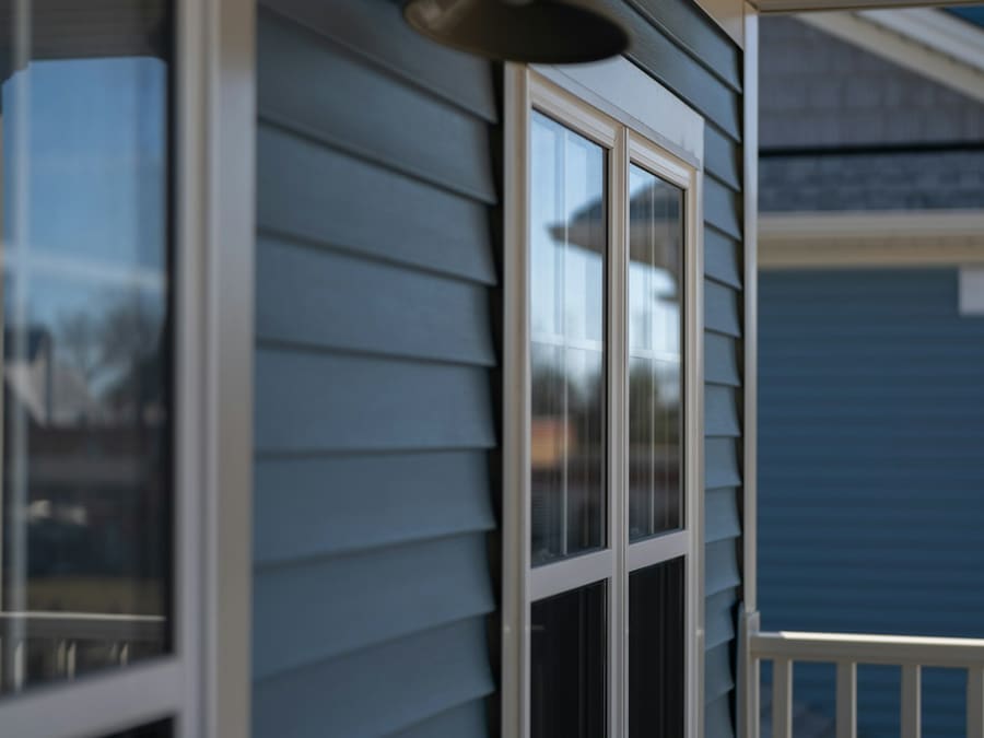 Mur extérieur en déclin horizontal bleu-gris avec cadrages de fenêtre blancs, sur une maison de banlieue
